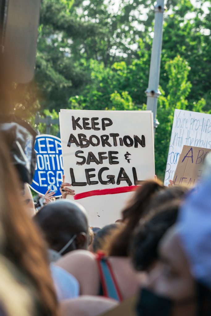 image of protest marches with a placard that says, "KEEP ABORTION SAFE & LEGAL"